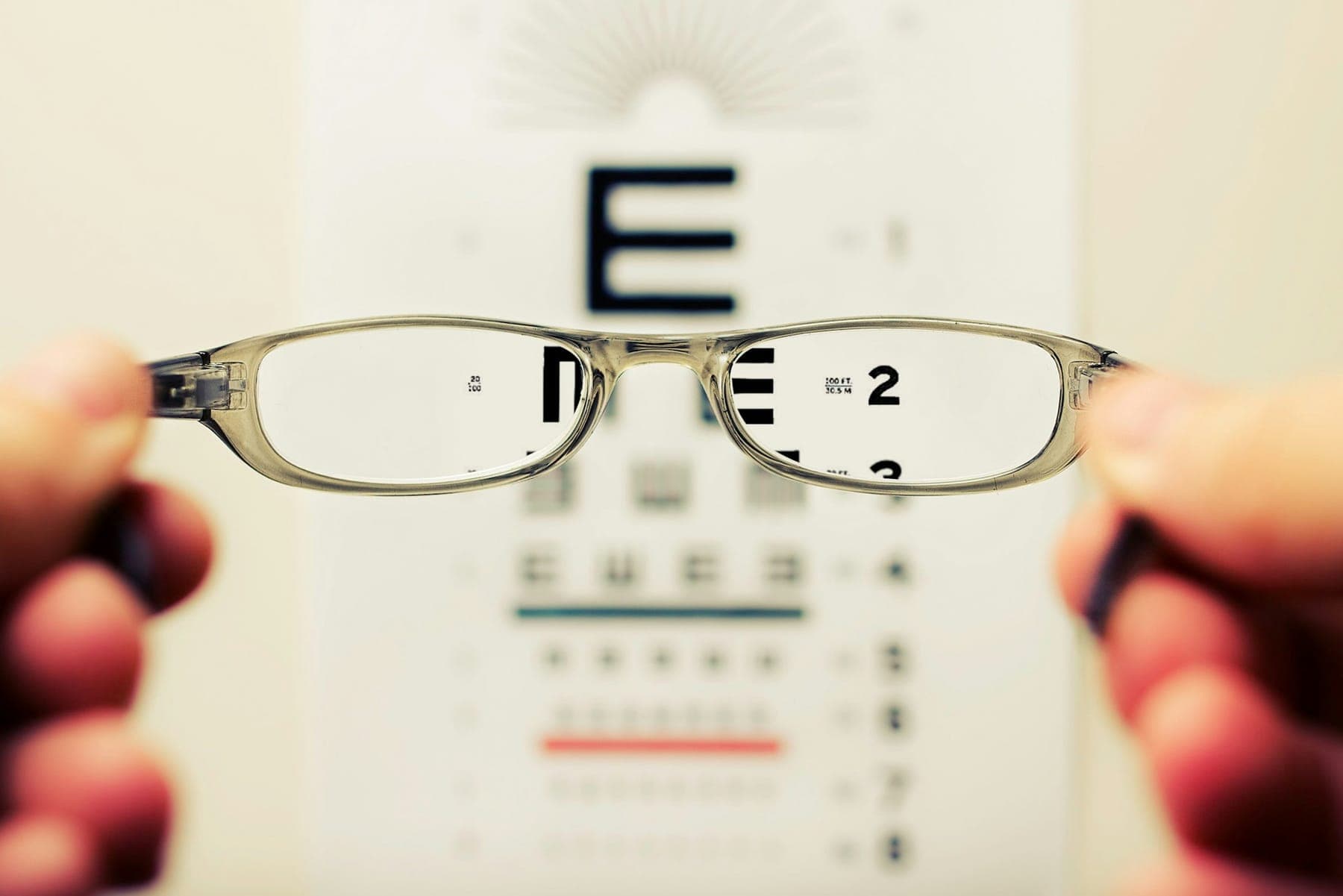 Hands holding glasses in front of an eye chart