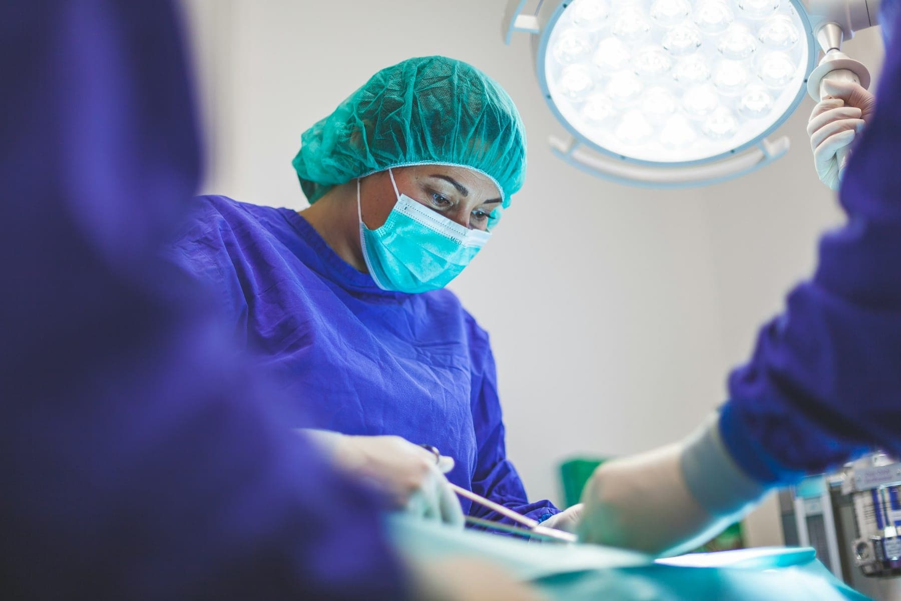 Surgeon in scrubs and cap operating under theatre lights