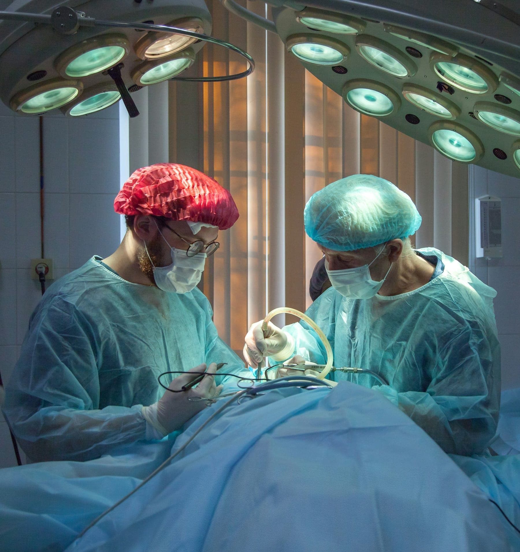 Two surgeons in scrubs operating under bright theatre lights